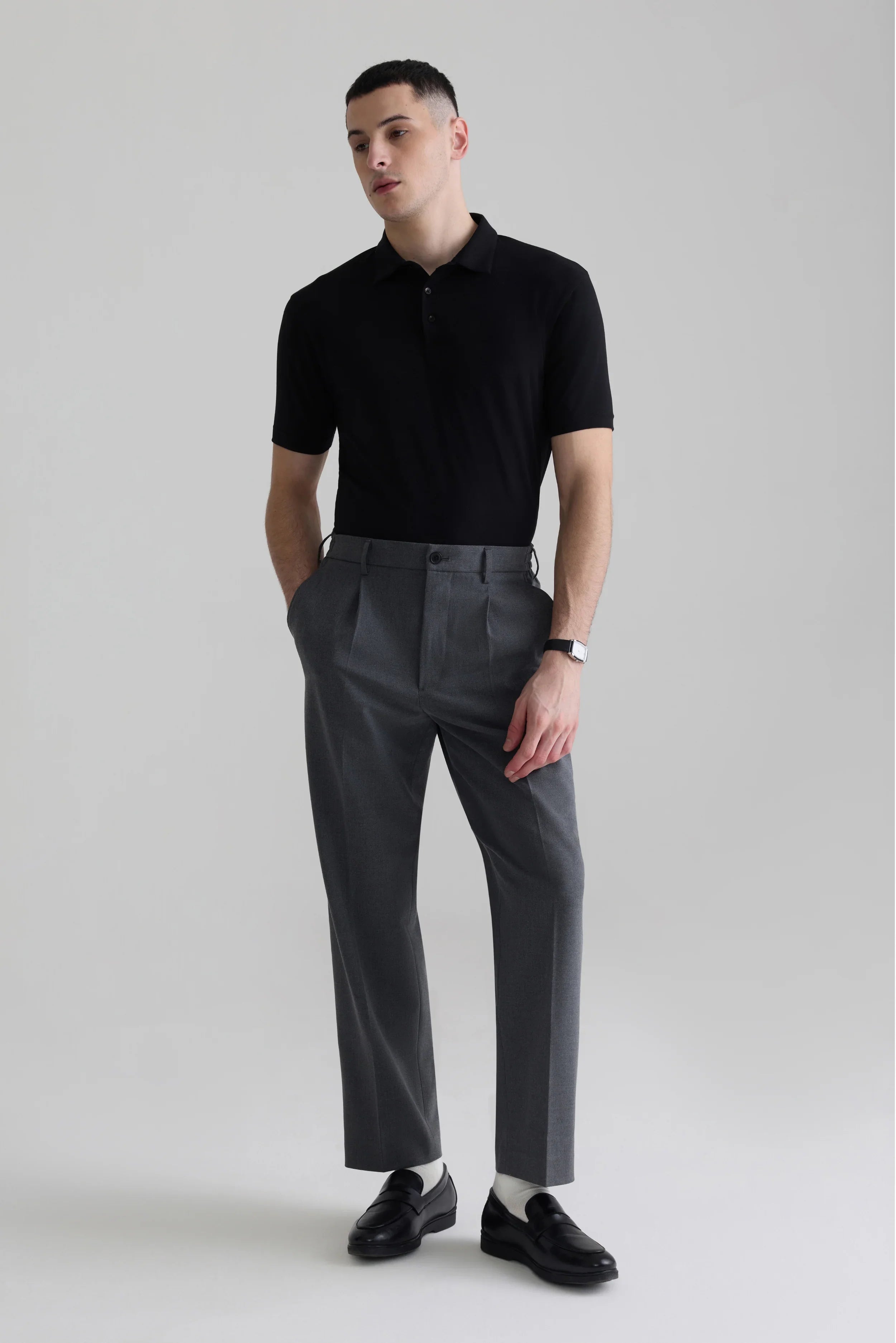 Man wearing black polo shirt and gray pleated trousers, minimalist style