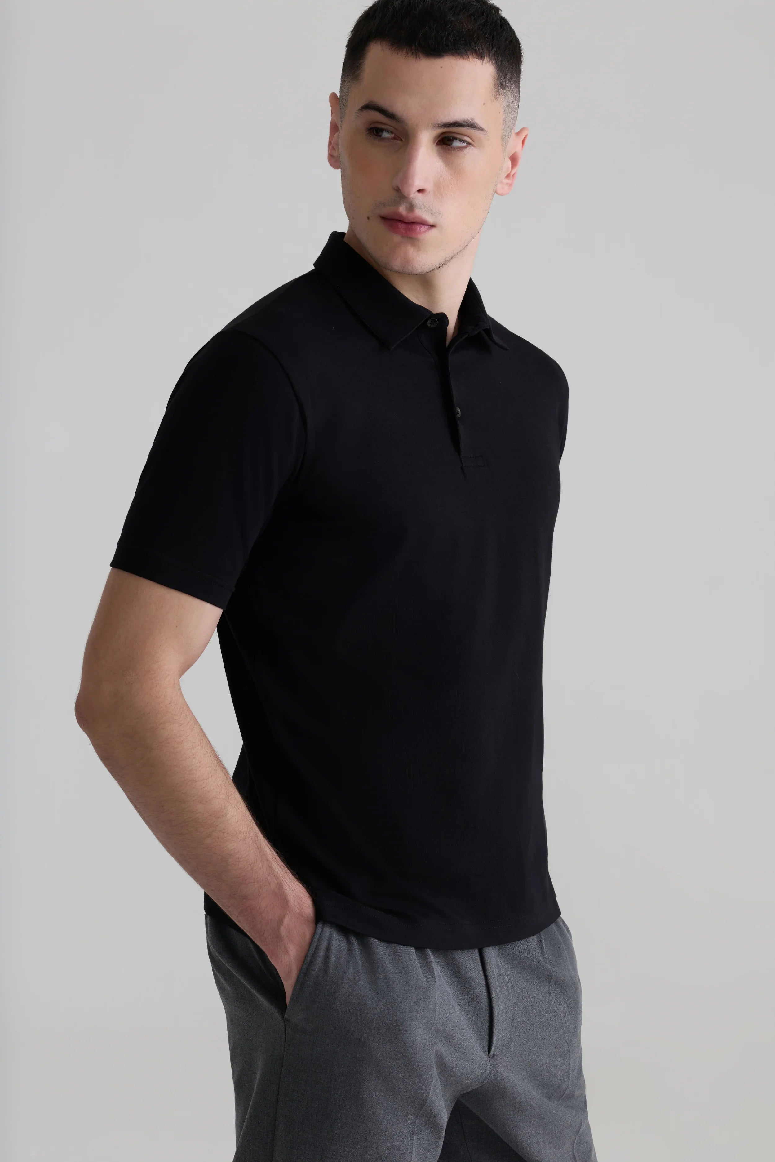 Men's black polo shirt with minimalist design, paired with gray trousers for a modern, functional look.